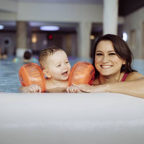 Mama und Kleinkind mit Schwimmflügel im Pool am Rand