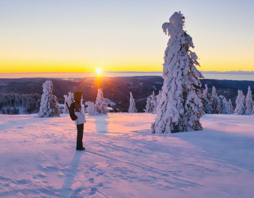 Wanderin steht im Schnee auf dem Felberg und betrachtet den Sonnenuntergang