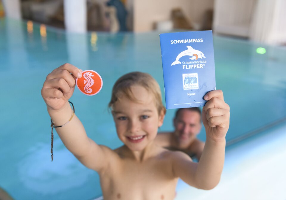 Junge hält Schwimmabzeichen in die Kamera