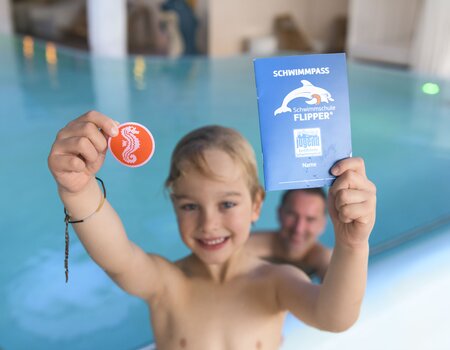 Junge hält Schwimmabzeichen in die Kamera