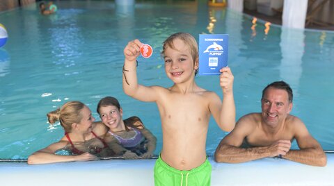 Junge hält Schwimmabzeichen in die Kamera